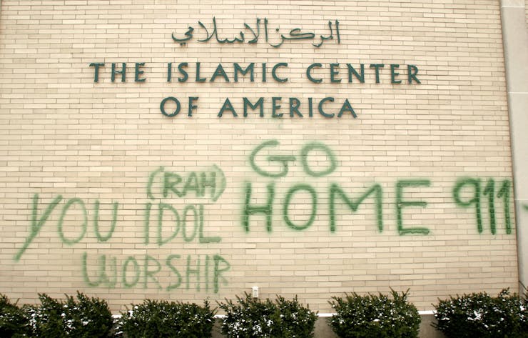 A beige wall that says The Islamic Center of America has graffiti on it that says 'Go Home 911' and 'You Idol Worship'