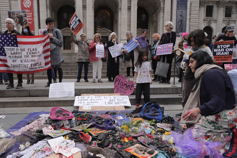 A group of people hold American flags and signs and stand near a collection of items spread on the ground.