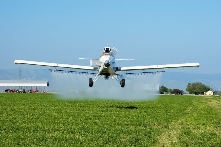 A plane flies lower over a field spraying a liquid from a bar of sprayers.