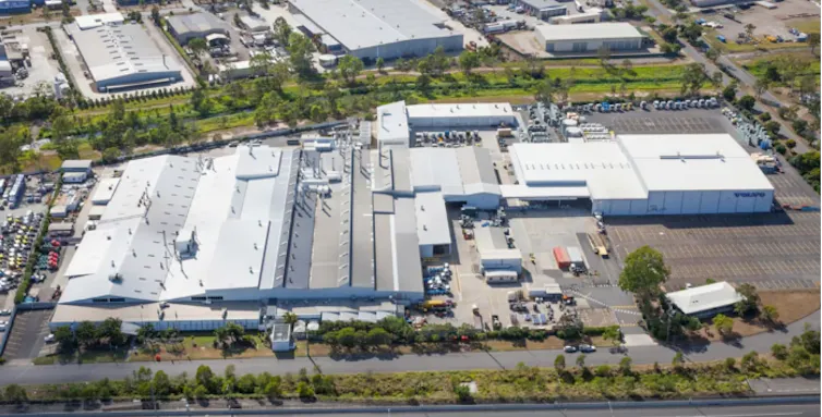 aerial shot of a truck factory, large industrial building surrounded by carparks and trees.