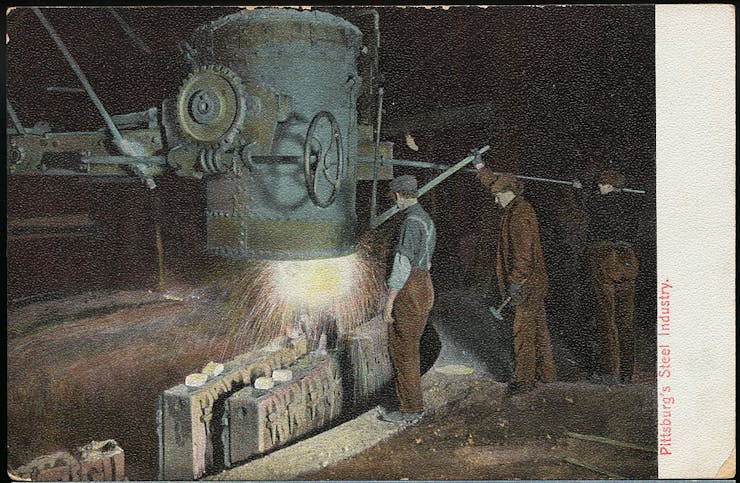 Three men wearing scally caps operate an old welding machine.