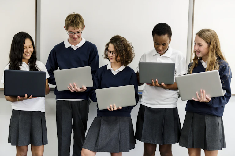 Five high school students in uniforms in a row, holding laptops.