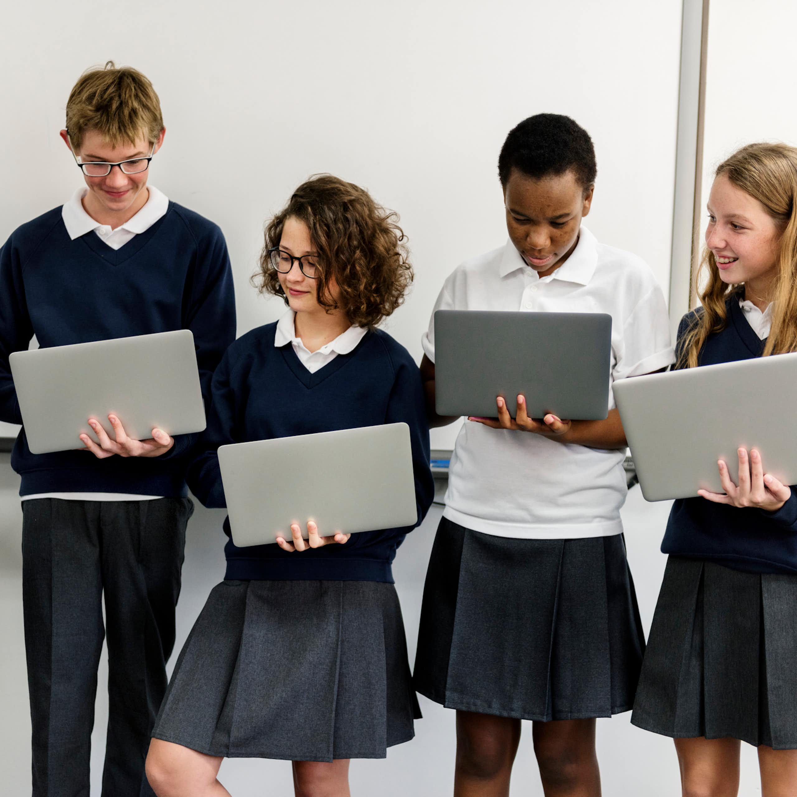 Five high school students in uniforms in a row, holding laptops.