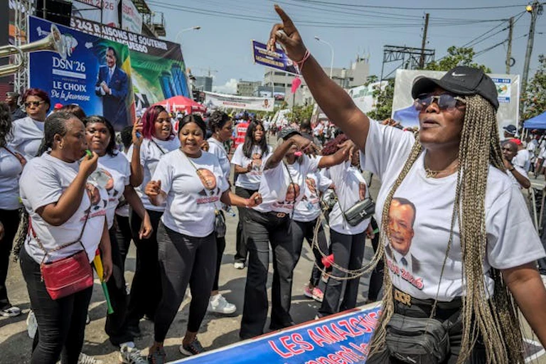 Women in a street, wearing T-shirts bearing a man's face