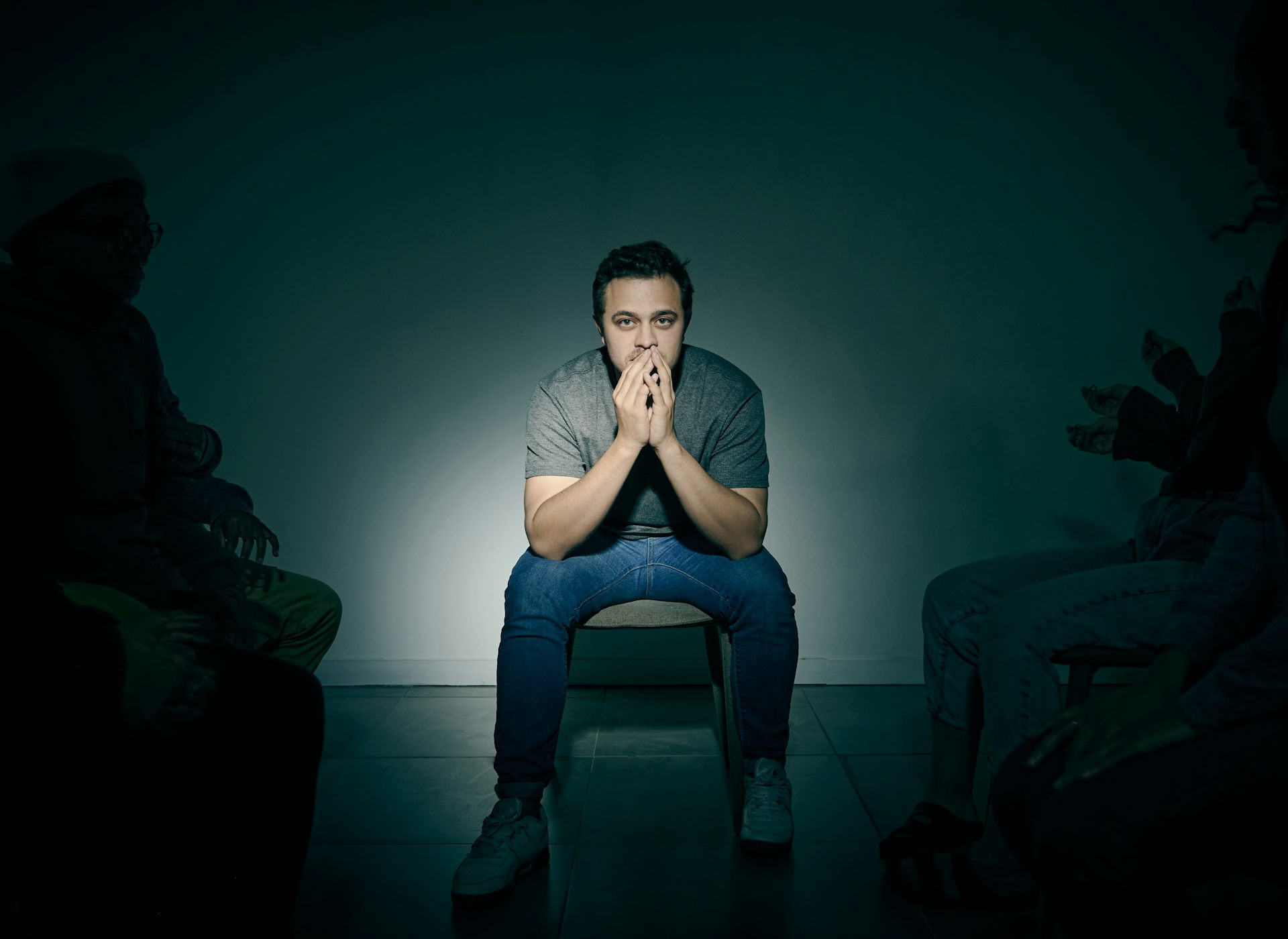 Un home sentat a una cadira, amb les mans tapant-se la boca i la mirada fixa. Hi ha molta gent al seu voltant.