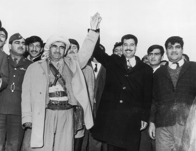 In a black and white photo, two men hold hands high in the air.