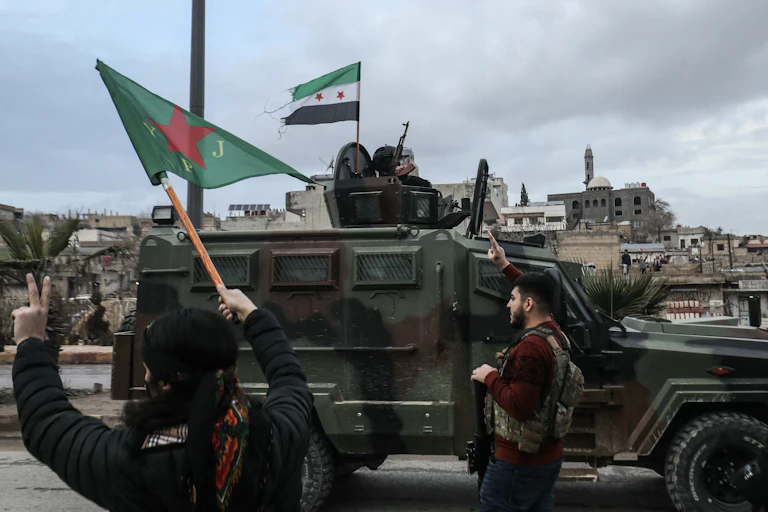 Two people gesture toward an approaching military vehicle.