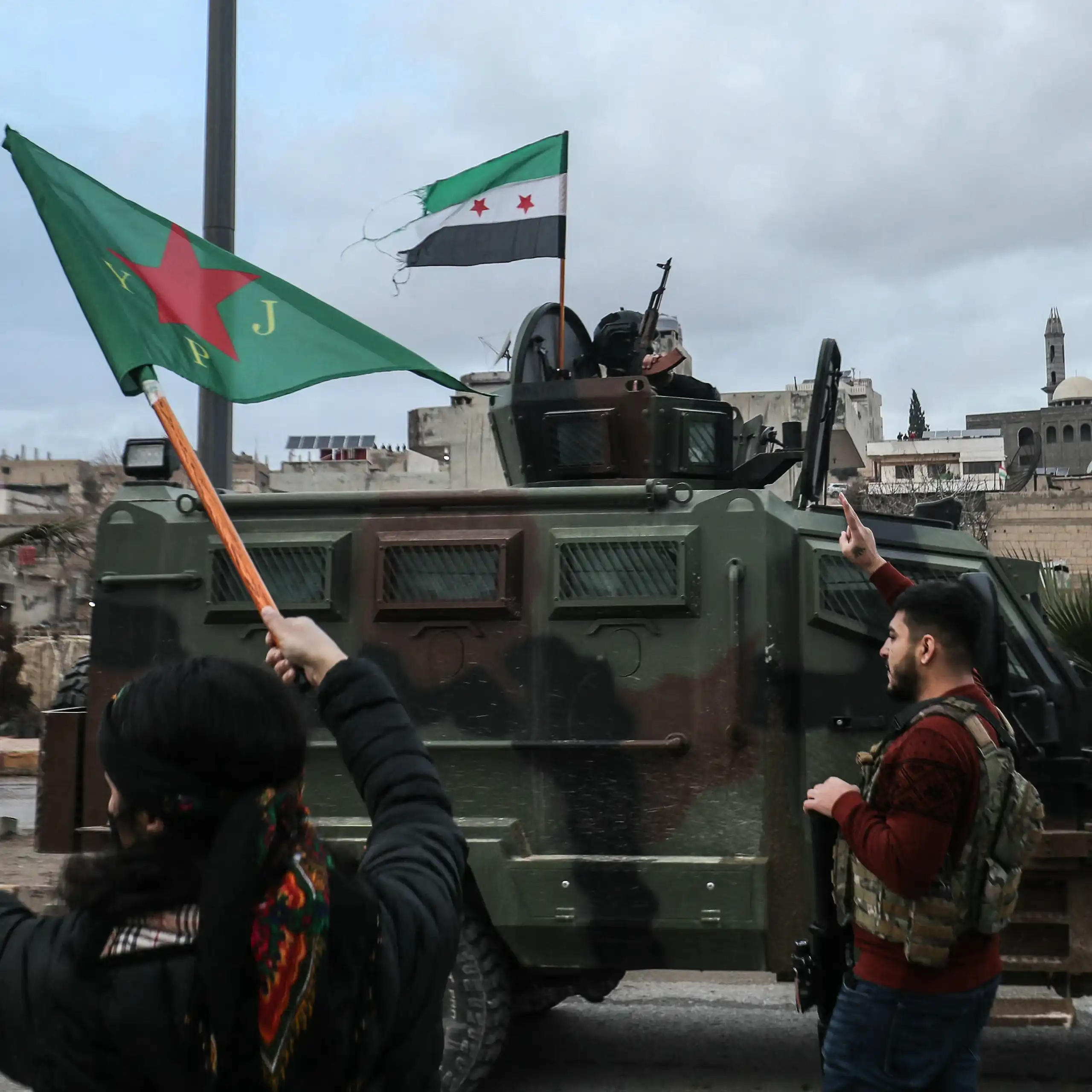 Two people gesture toward an approaching military vehicle.