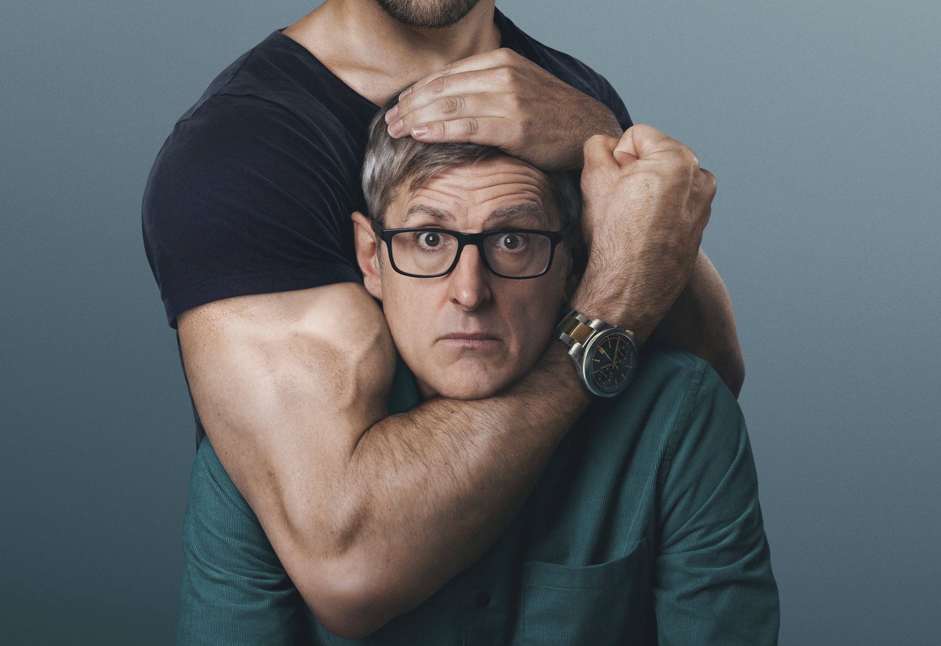 A speccy nerdy-looking guy in a headlock by a guy with massive muscles.