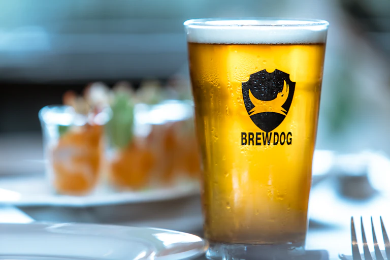 branded pint glass of brewdog beer with other glasses blurred in the background.