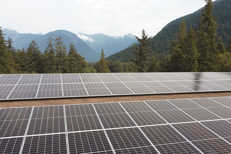 Solar panels on a roof are seen at the bottom of the photo, with mountains, forest and sky in the background above.