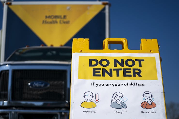 A sign in front of a mobile health vehicle asks people not to enter if they are experiencing measles symptoms.