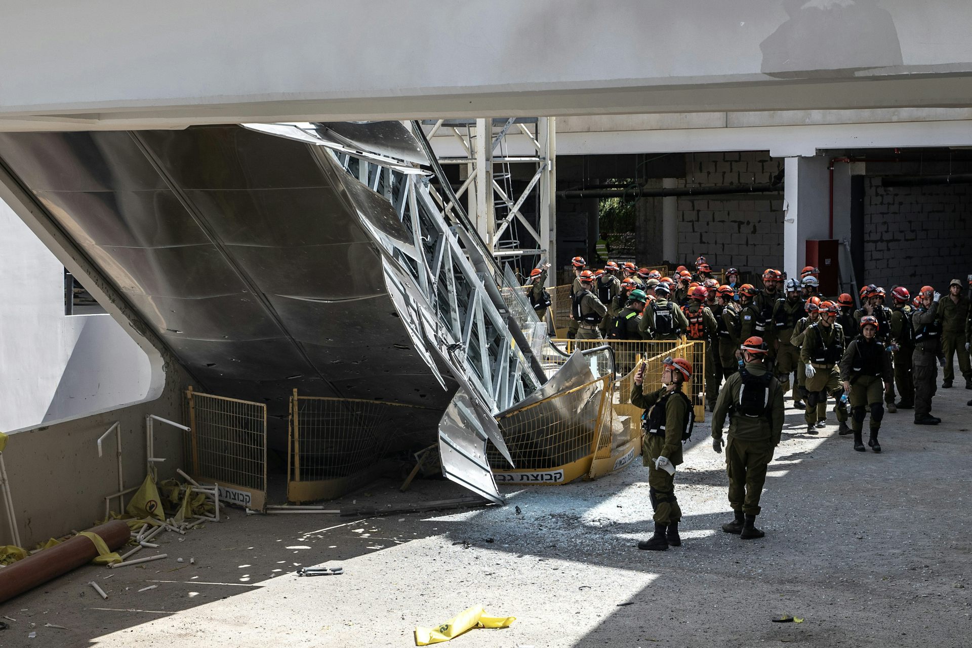 Un grupo de uniformados se reúne cerca de una gran estructura de acero derrumbada que parece ser parte de un puente.