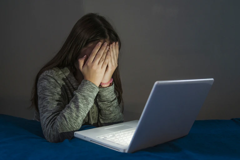 Une adolescente se cache les yeux devant un écran d’ordinateur