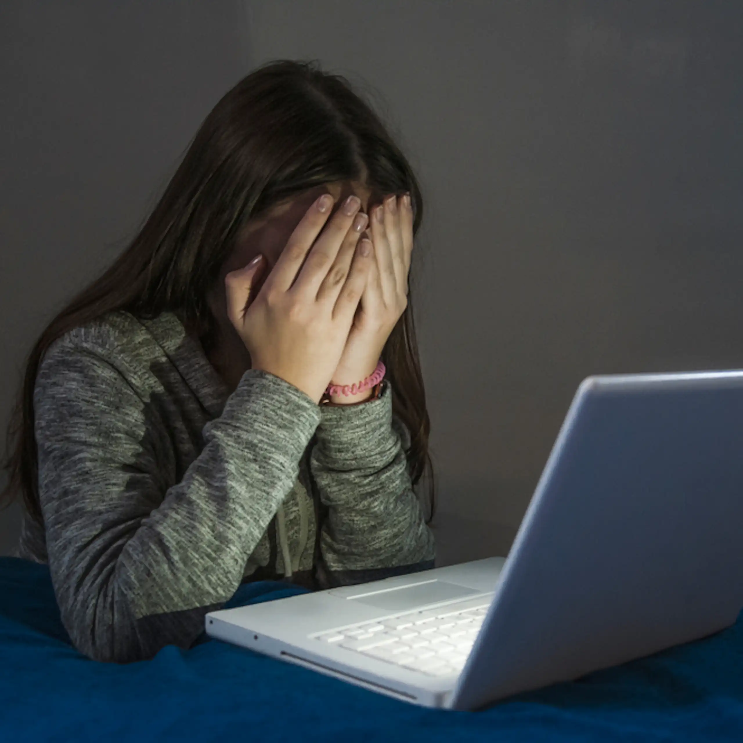 Une adolescente se cache les yeux devant un écran d’ordinateur