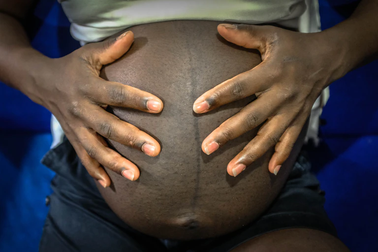 A heavily pregnant young woman touches her baby bump