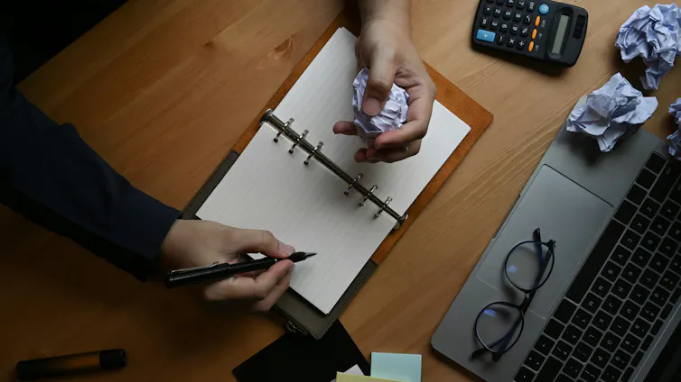 A hand crumpling papers on a desk.