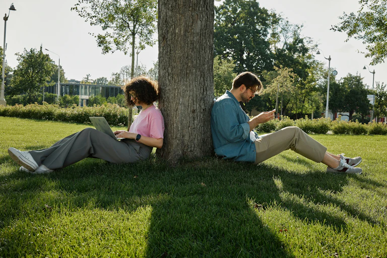 Two people sitting with their backs to a tree.
