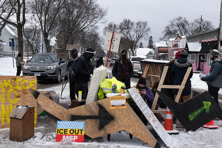 Four masked individuals directing traffic around a makeshift barricade in the road.