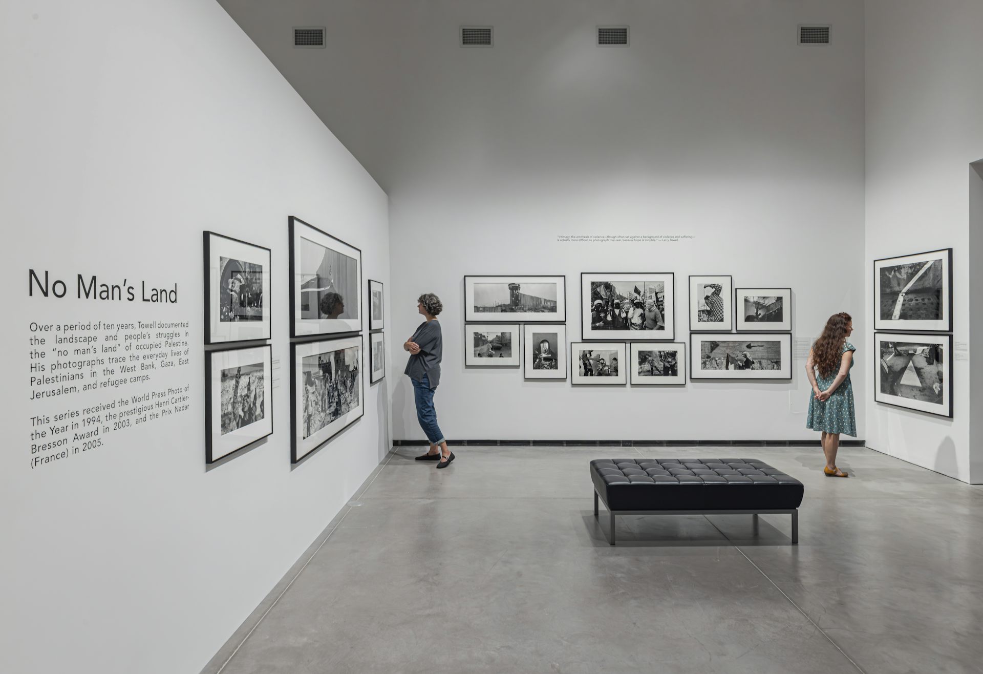 Vista de instalación de dos mujeres mirando fotografías en una galería de arte.