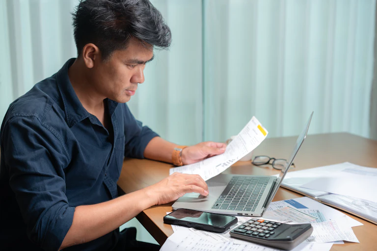 Middle-aged man reviewing a financial document in front of his laptop.