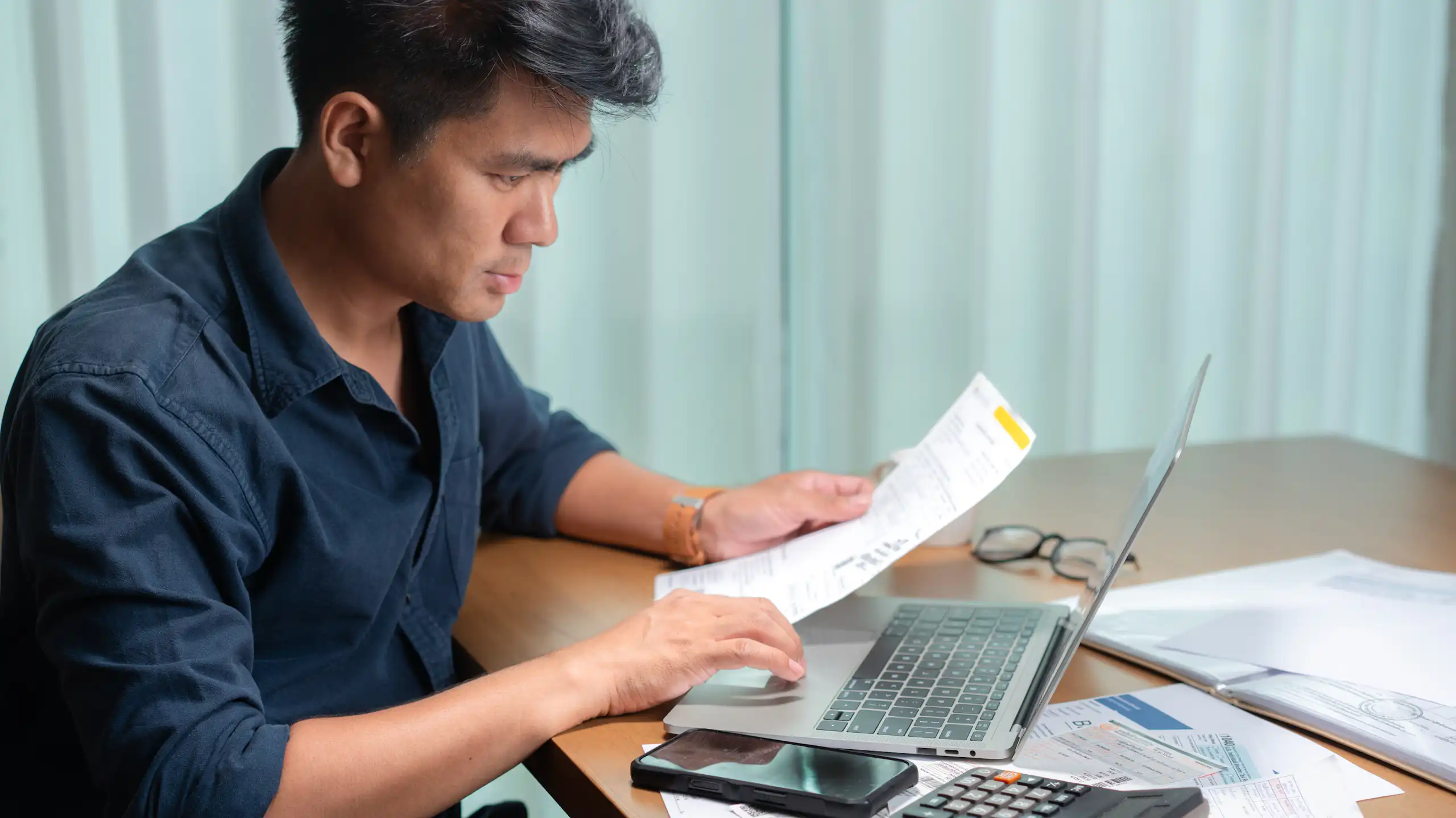 Middle-aged man reviewing a financial document in front of his laptop.