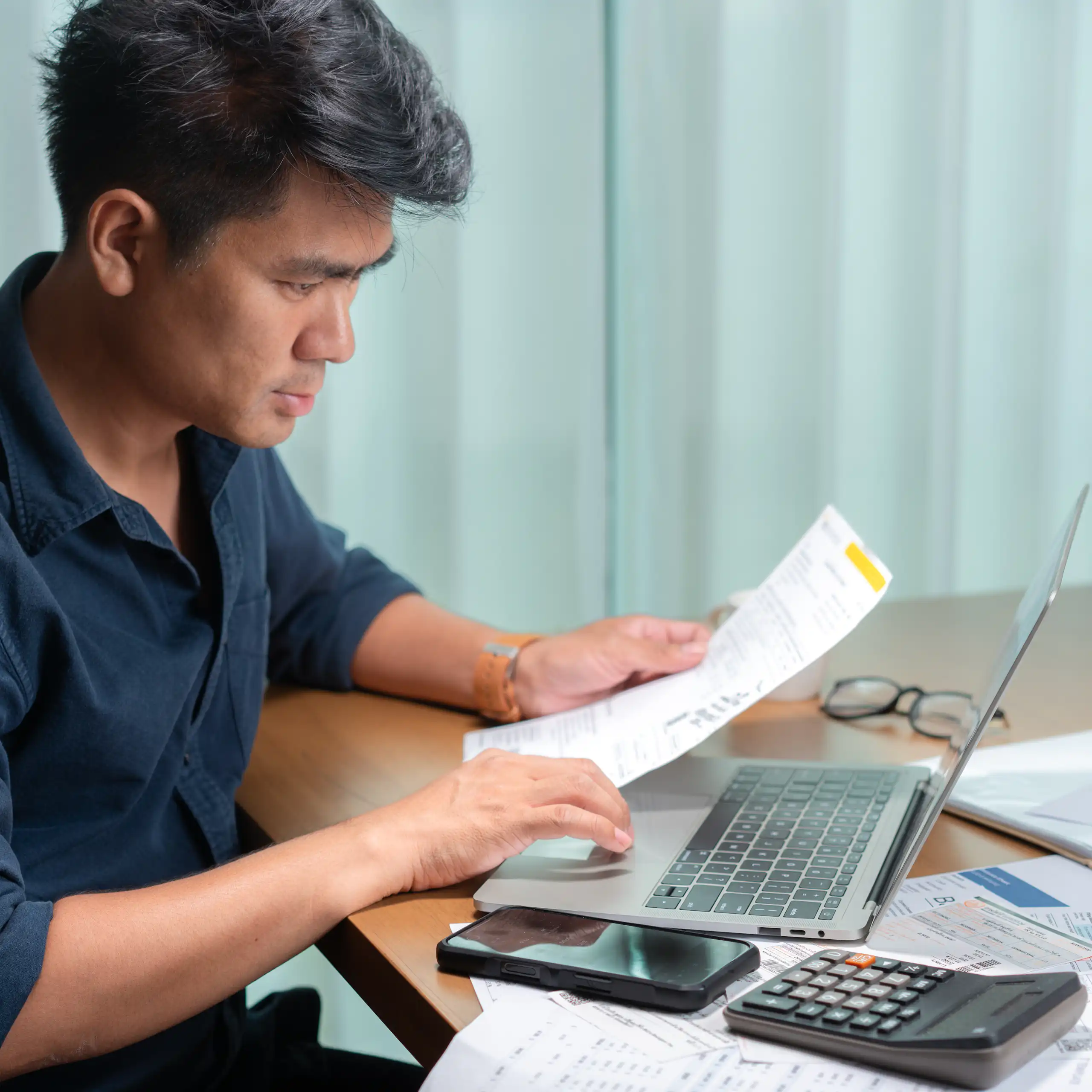 Middle-aged man reviewing a financial document in front of his laptop.