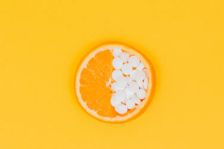 An orange with half holding vitamin C tablets
