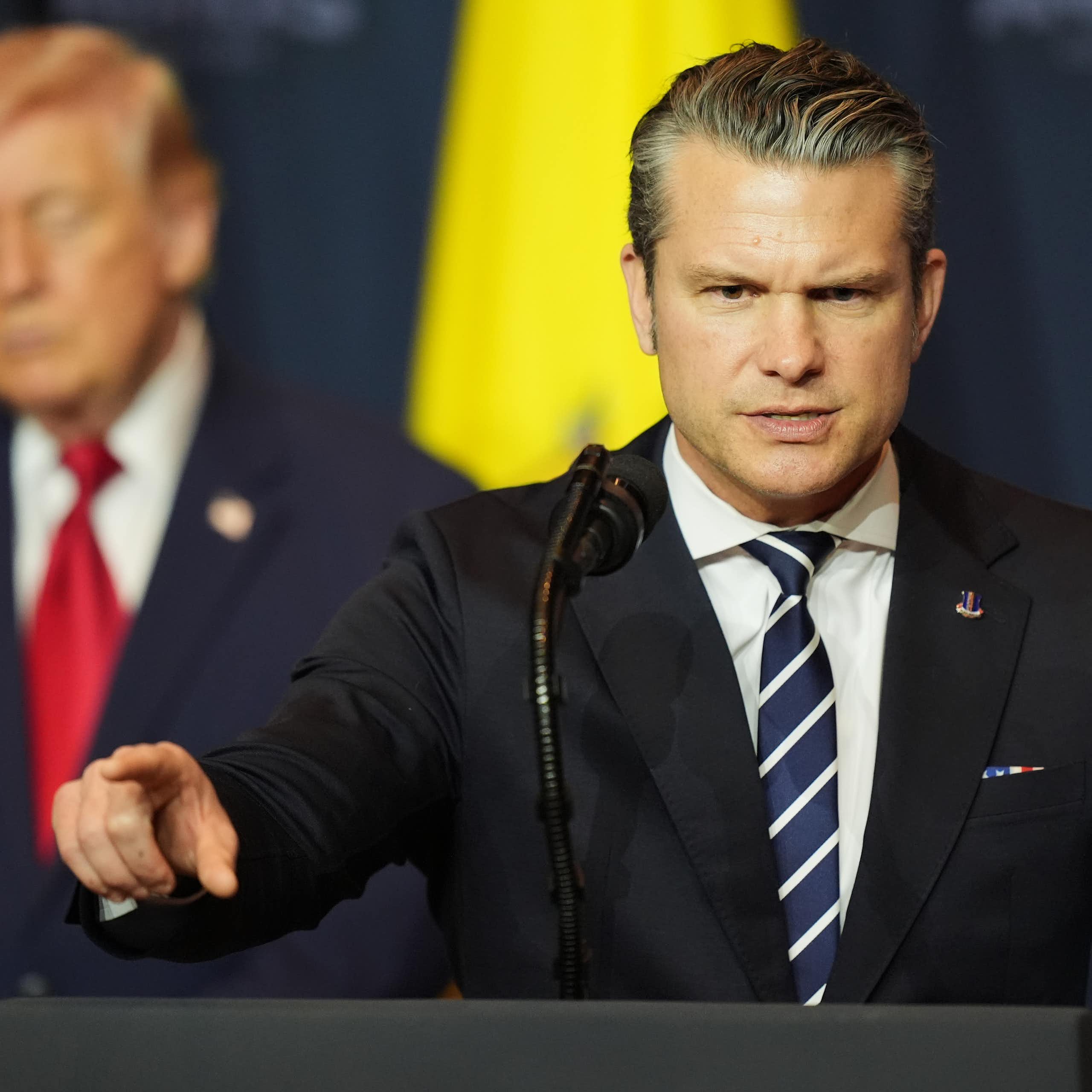 an angry Pete Hegseth at podium, Donald Trump behind him