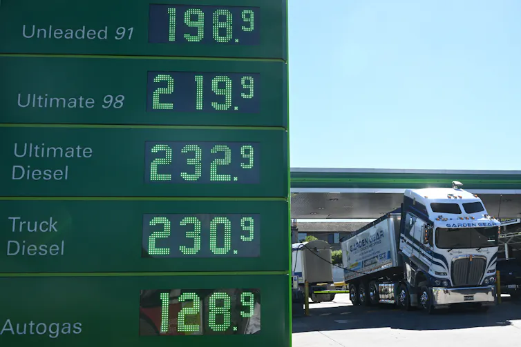 fuel prices sign in foreground at service station, with truck refuelling behind.