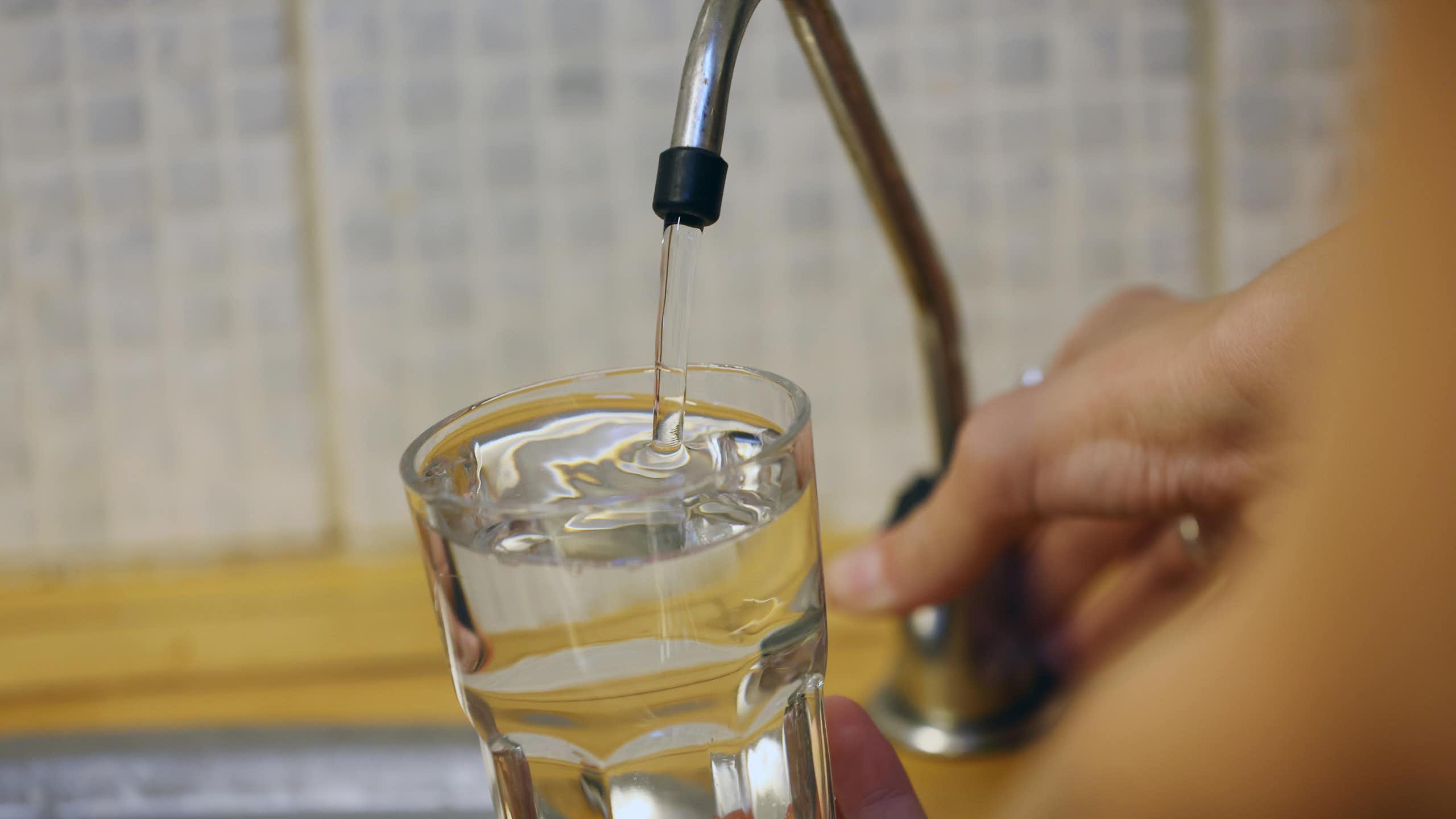 A person fills a glass with water from a tap.