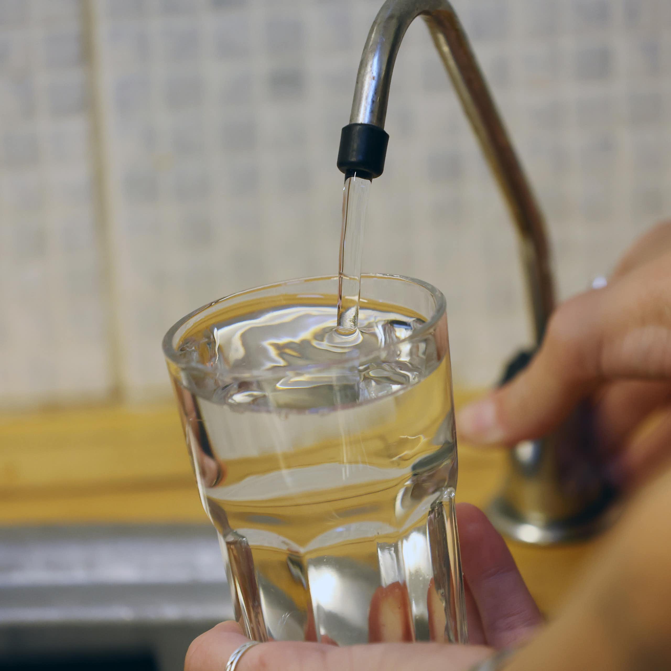 A person fills a glass with water from a tap.