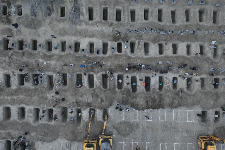 An aerial view shows a mass grave site, with some people looking over the rows of empty graves.