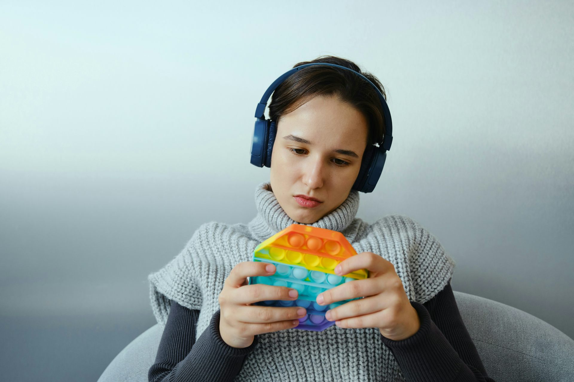 A girl wearing headphones and playing with a multicoloured bubble popper fidget toy