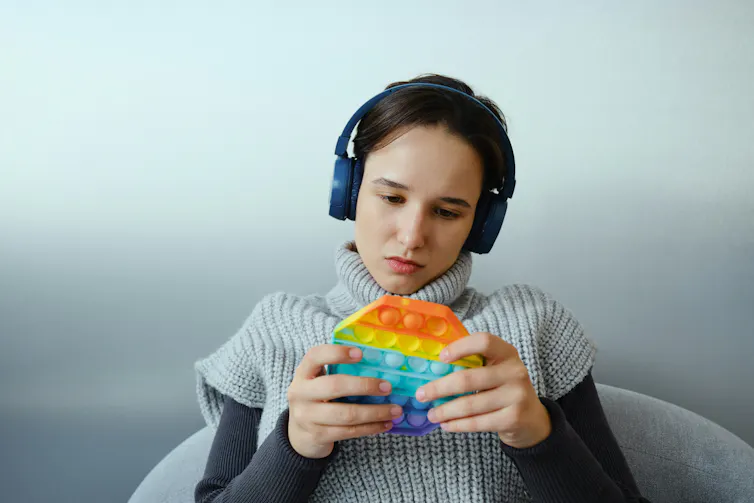 A girl wearing headphones and playing with a multicoloured bubble popper fidget toy