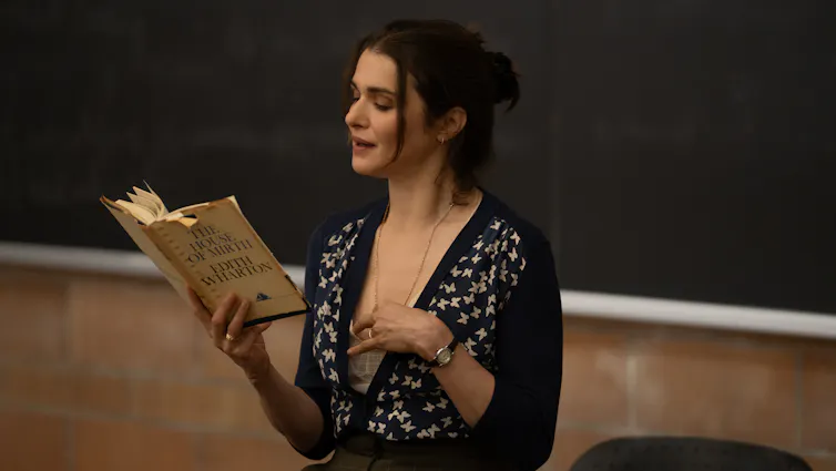 a woman reads from a book at a blackboard
