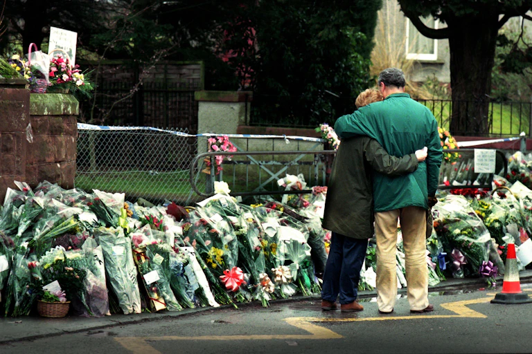 A couple embraces outside piles of flowers at Dunblane school