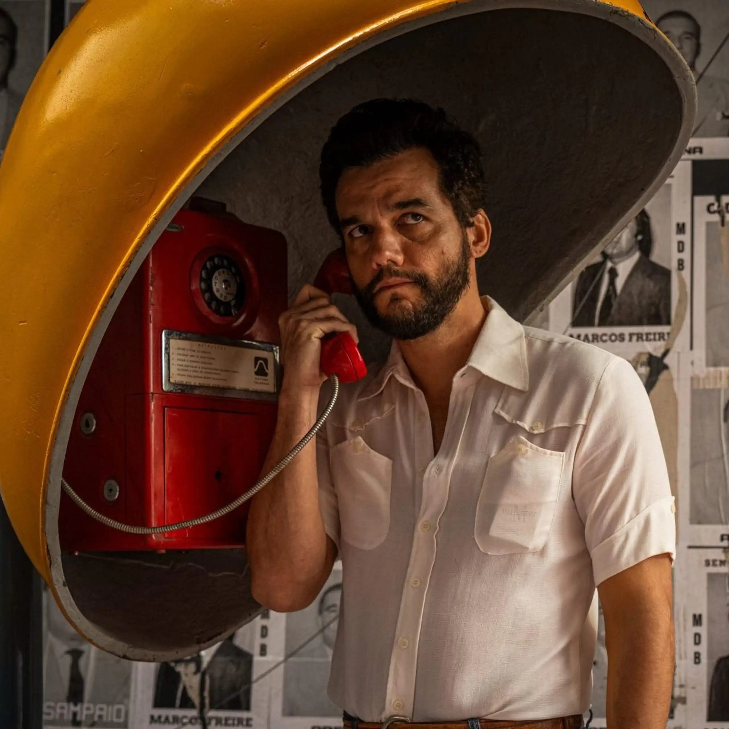 Un hombre con camisa habla desde una cabina telefónica.