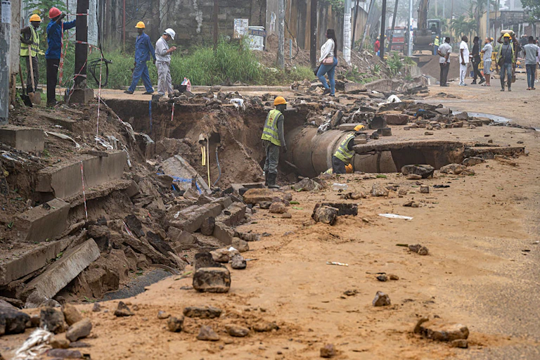 Workers in hard hats looking at a road that has been damaged
