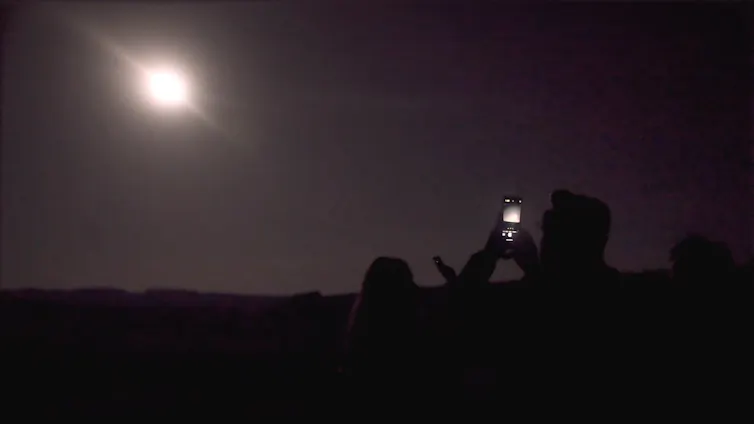 A person holding up a phone to take a photo in the dark.