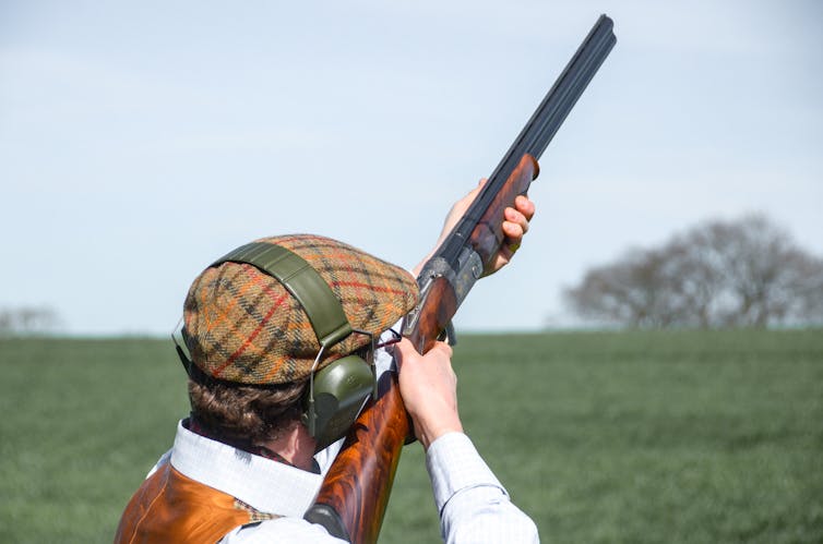 A man in posh hunting clothing shooting a shotgun into the air