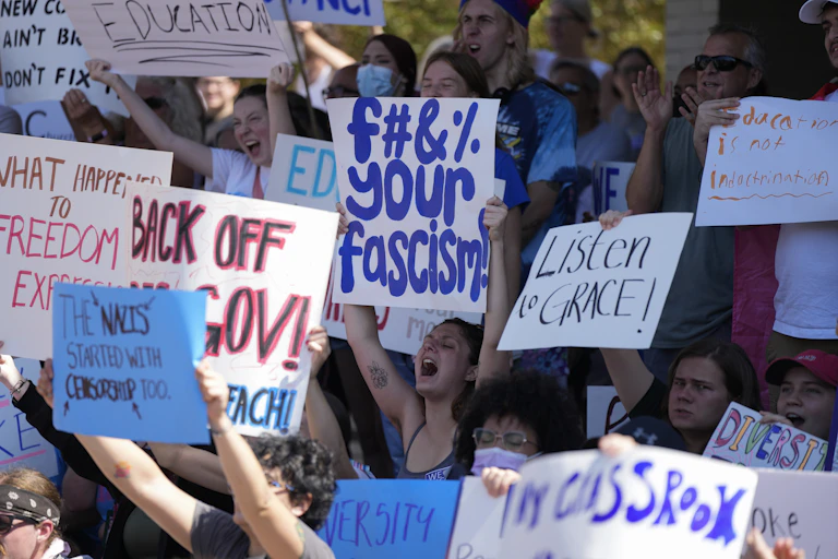 Students hold up protest signs, one reading 'F Your Fascism.'