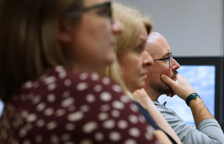 Three people are seen from the side, looking forward in the same direction.