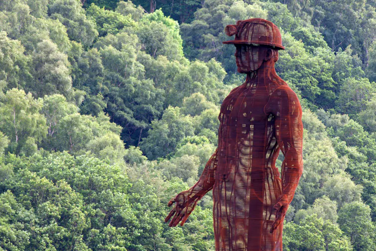 A large red metal sculpture of a coal miner against the backdrop of a green forest