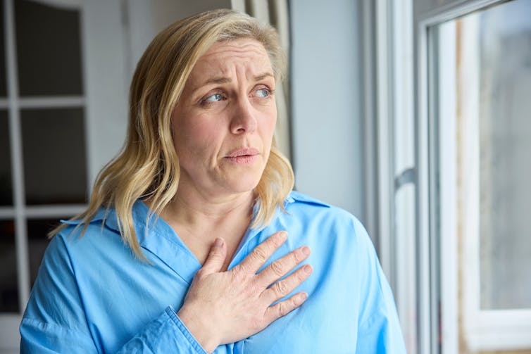 Woman standing by window with hand on heart, looking worried