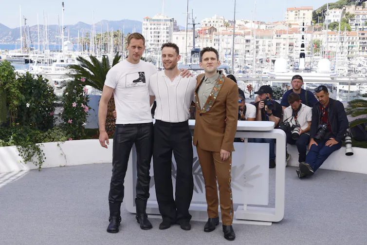 Three men with their arms around each other while a lot of photographers photograph them.