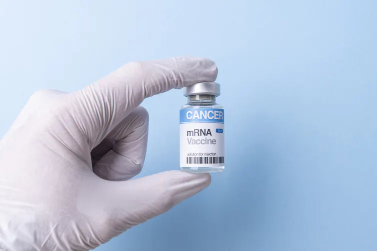 Hand wearing white nitrile glove holding a vial labeled (CANCER mRNA vaccine) between two fingers