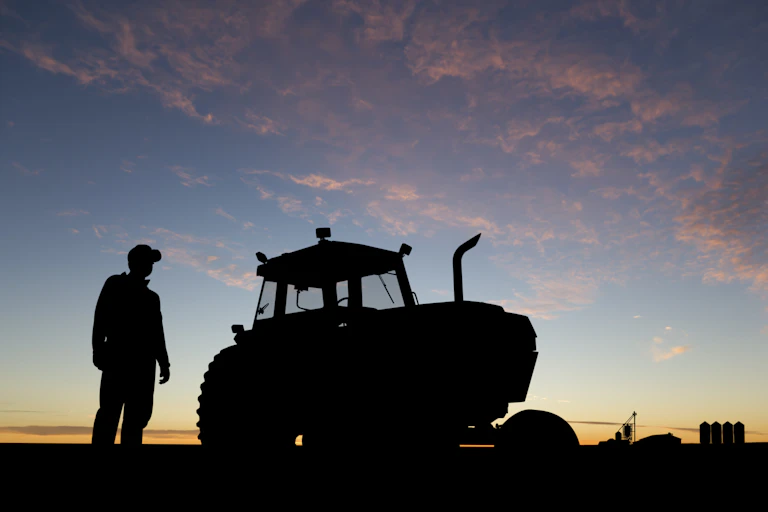 silhouette of a farmer and a tractor against the sky