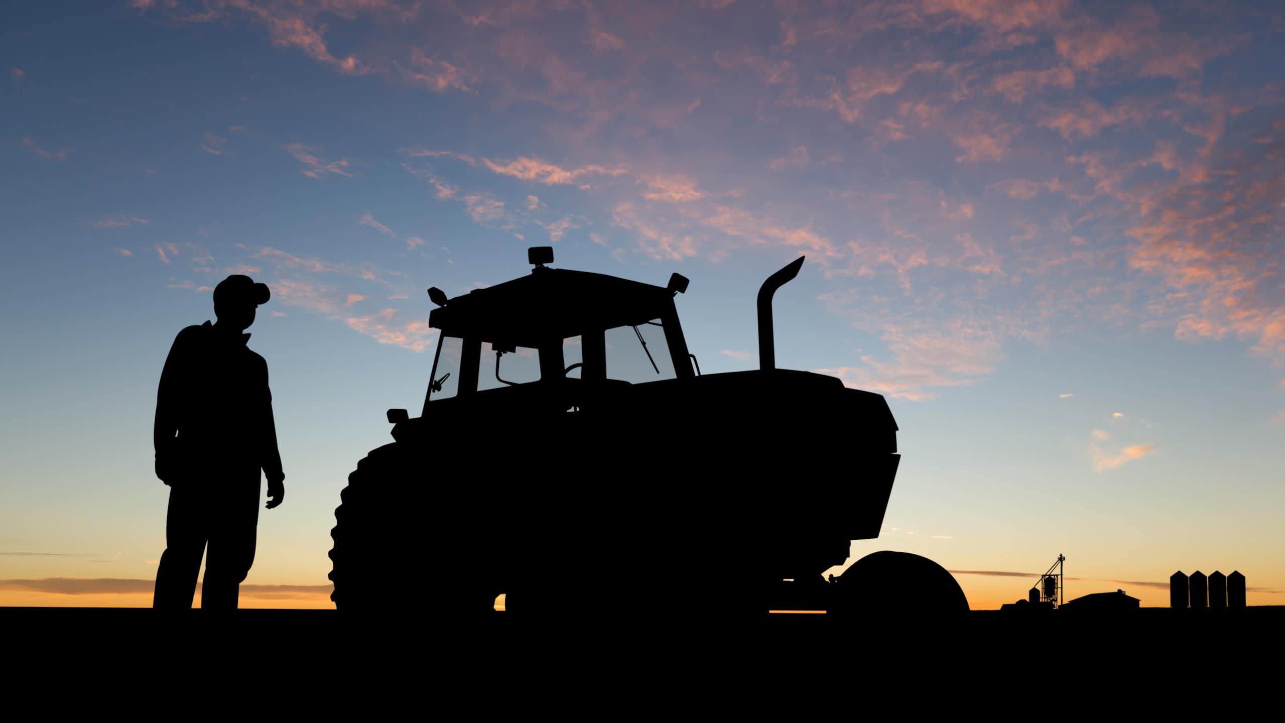 silhouette of a farmer and a tractor against the sky