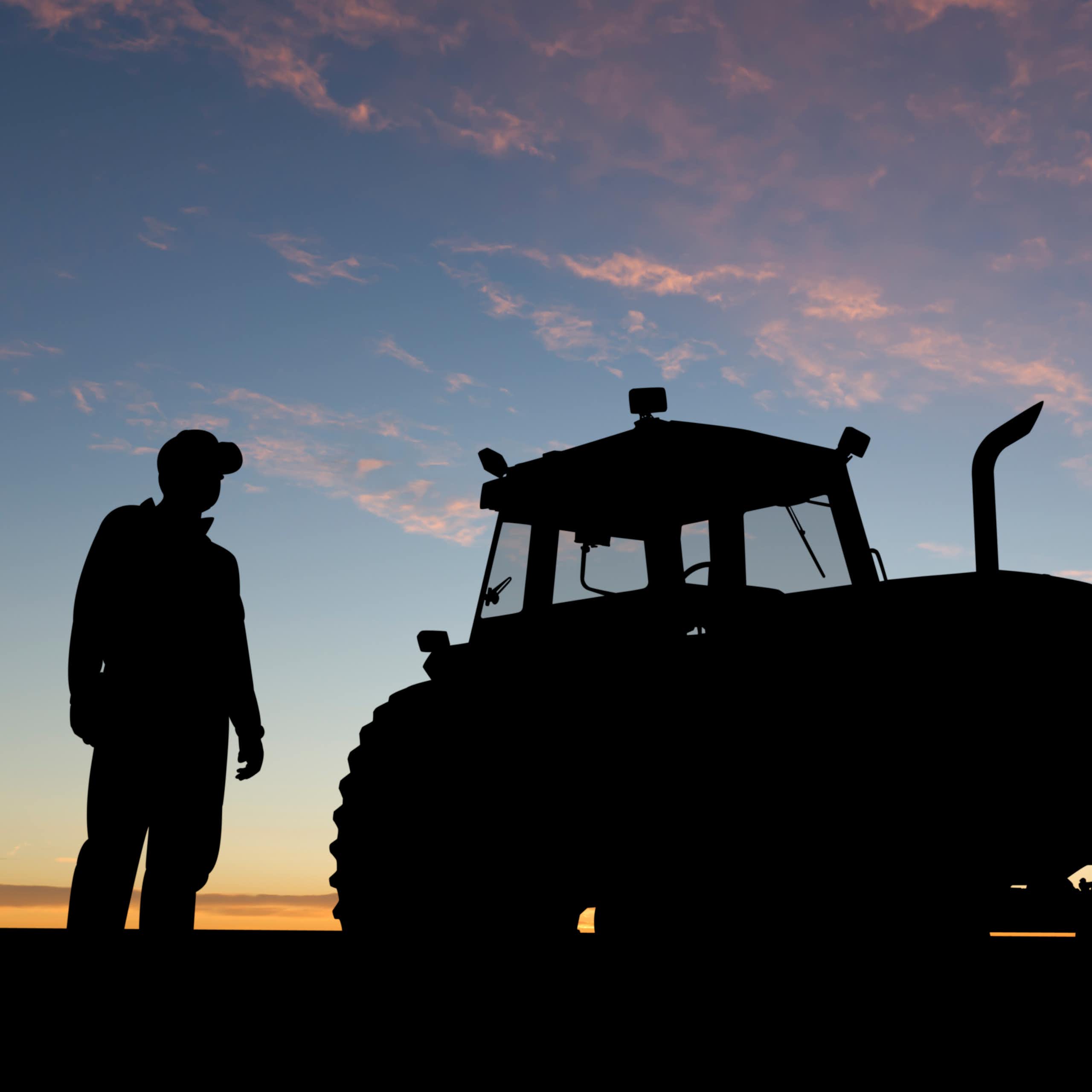 silhouette of a farmer and a tractor against the sky